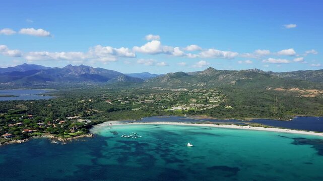 A stunning aerial view of Spiaggia Lu Impostu beach near San Teodoro, Sardinia, Italy. The landscape includes both the beach and the surrounding countryside, with residential areas visible.