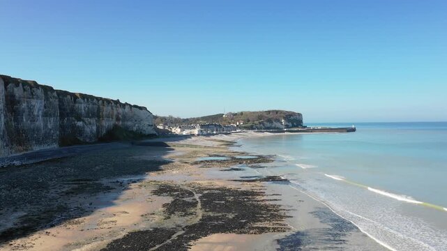 Wide shot of the dramatic white chalk cliffs and sandy beach at Saint-Valery-en-Caux on the Normandy coast of France. No people are visible, emphasizing the peaceful and natural atmosphere.