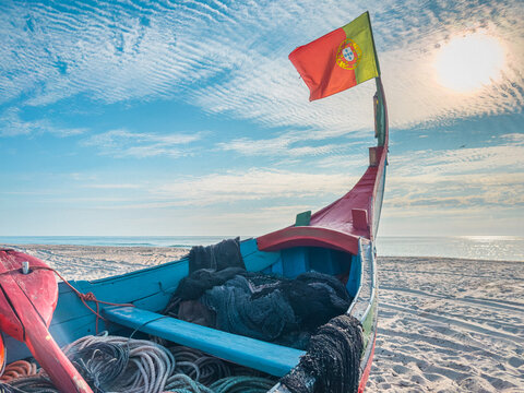 Traditional Portuguese fishing boat with national flag on sunny sandy beach