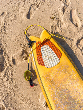 Yellow fish surfboard with leash resting on sandy beach