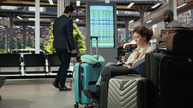 Woman scrolls on a smartphone beside packed baggage in a bus station before departure, using the phone in the shuttle terminal while traveling with many bags.
