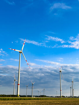 Wind turbines stand tall in open field. Large wind turbines turn slowly under a clear blue sky in a rural area during daylight.