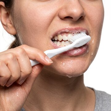 A woman brushing her teeth vigorously with a toothbrush, foam and water dripping from her mouth. Her expression shows concentration and perhaps a slight grimace