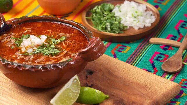 Traditional Mexican birria stew in a handmade clay bowl garnished with chopped cilantro and onion served with lime wedge