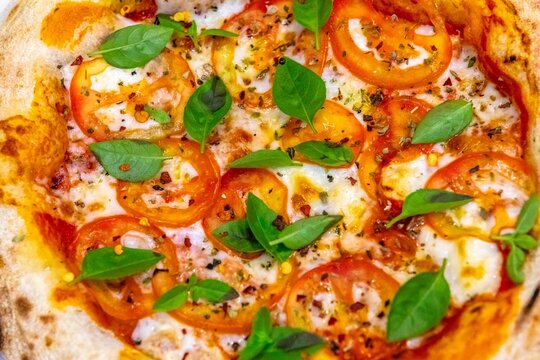 Neapolitan-style personal pizza with naturally leavened long-fermentation dough, sliced tomatoes, melted mozzarella, fresh basil and oregano, served on a white plate over a dark pinstriped cloth.