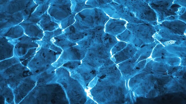 Deep blue water surface with bright white caustic light patterns and gentle undulating ripples. Abstract swimming pool or ocean texture.