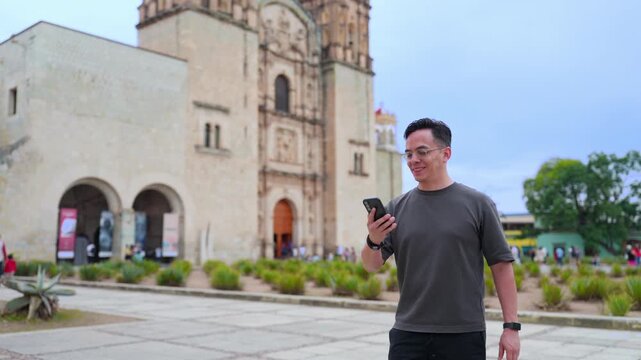 Young man exploring a latin american city, happily using his smartphone to take pictures of the templo de santo domingo de guzman in oaxaca, mexico during his vacation