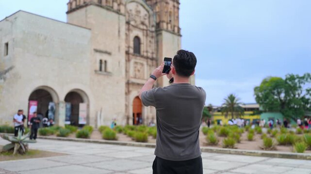 Young man using a smartphone to take a photograph of the templo de santo domingo de guzman, a historic landmark and tourist attraction in oaxaca de juarez, mexico, during his vacation