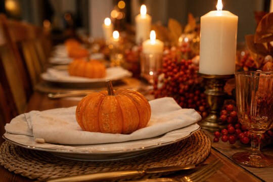 Thanksgiving table setting with automnal decorations, pumpkins, glasses and plates. Holidays, catering and hospitality concept.