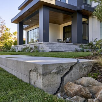 Modern home exterior with a cracked concrete patio foundation highlighting structural damage and natural landscaping in a sunny residential setting