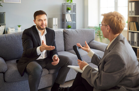 Businessman in interview speaks into microphone with journalist. He has focused conversation with interviewer in office. Woman interviewing guest. Concept media communication and corporate dialogue.