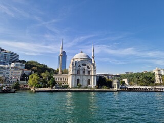 Naklejka premium Dolmabahce Mosque on the Bosphorus strait shore with blue water and clear sky in Istanbul, Turkey