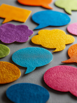 Vibrant multicolored paper speech bubbles scattered on a neutral surface symbolizing communication, dialogue, and diverse conversations in social settings or teamwor