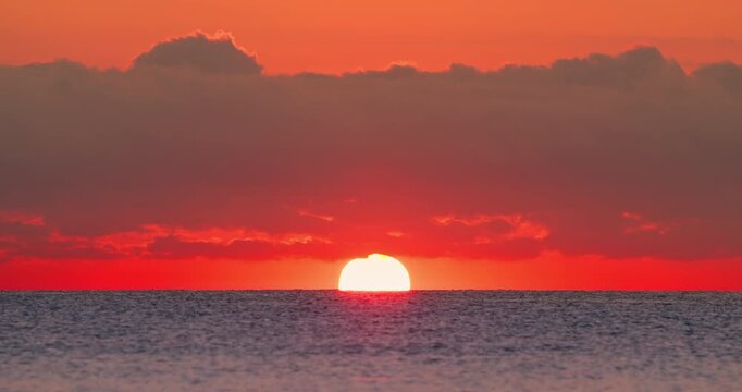 Scenic golden sunrise over the ocean horizon with sun rays reflecting on calm water. Beautiful dramatic sky during morning dawn