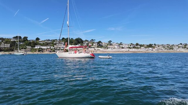 St Mawes Cornwall England UK. 13.08.2026. Video. A serene view of a sailboat moored in clear blue water with a charming white-washed village of St Mawes nestled on the hillside under a bright sky