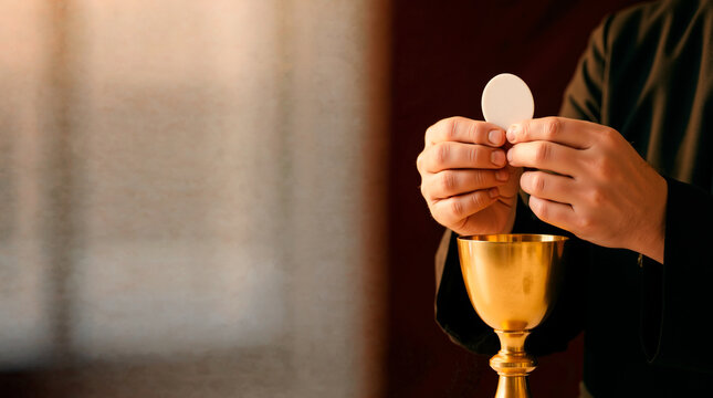 Hands of a priest holding a white communion wafer above a golden chalice. Holy Eucharist sacrament in a church. Christian religious ritual with copy space