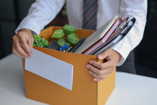 Business professional holding resignation letter and packed of personal belongings in cardboard on a desk. Concept of job resignation or termination.