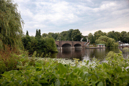 Arched stone bridge crossing an Alster waterway surrounded by lush summer vegetation in Hamburg, Germany.
