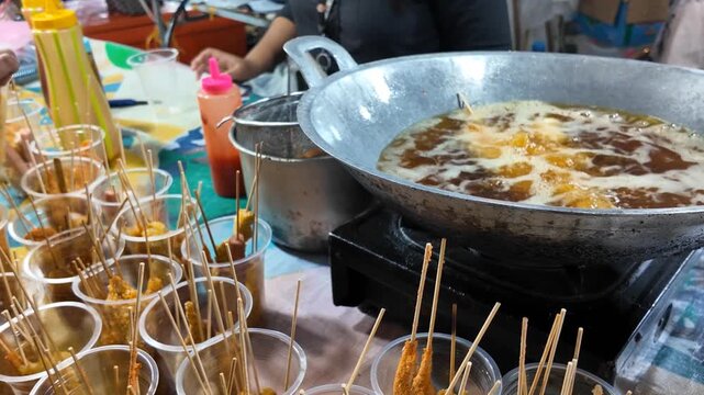Golden skewers sizzle in hot oil as the street vendor carefully prepares fresh snacks, filling the night air with irresistible aromas.