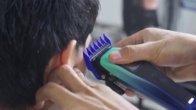 Professional barber cutting man's hair with electric clipper