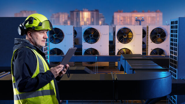 HVAC engineering. Technician uses a tablet to inspect rooftop air conditioning units, ventilation equipment and commercial building cooling systems.