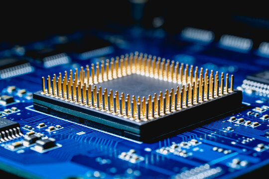 A close-up view of a pin grid array integrated circuit mounted on a blue printed circuit board, showing gold-plated pins and surrounding electronic components.