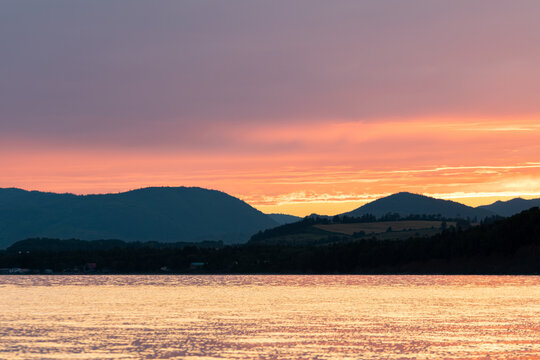 Gaspesie, Canada, 20 August 2026 : Vibrant sunset colors illuminate the sky above silhouetted mountains and reflect on the calm water