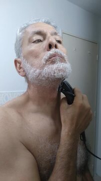 Mature man trimming and shaping his white beard and mustache with an electric clipper