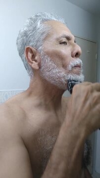 Mature man trimming and shaping his white beard and mustache with an electric clipper