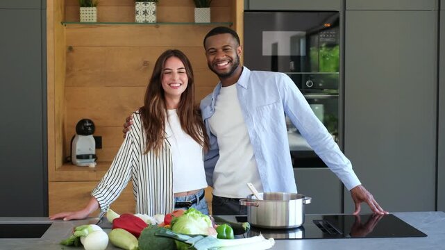 A joyful multi-ethnic couple shares a happy moment, preparing healthy vegetables for a meal in their stylish, modern kitchen. They are smiling, enjoying their time cooking together at home.