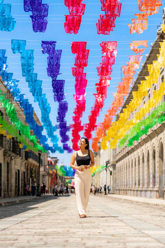 Latina woman strolling under vibrant papel picado banners in oaxaca, mexico, smiling and looking up while exploring colorful historic streets on a sunny cultural festival day