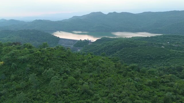 Aerial forward flight over dense forested mountains of Margallah towards Simli Dam and reservoir, Lake in a lush green landscape