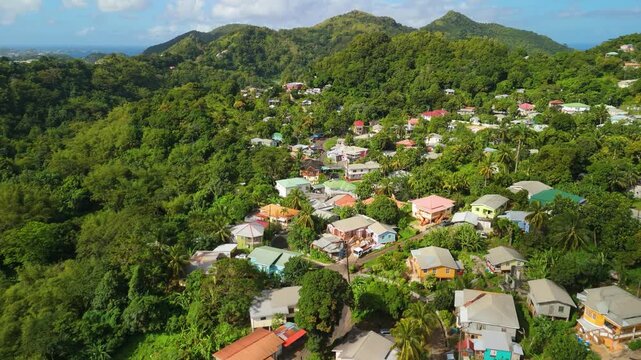 Aerial flight moves forward over Willis, Grenada, with lush tropical vegetation, colorful homes, hillside roads, and mountainous landscape