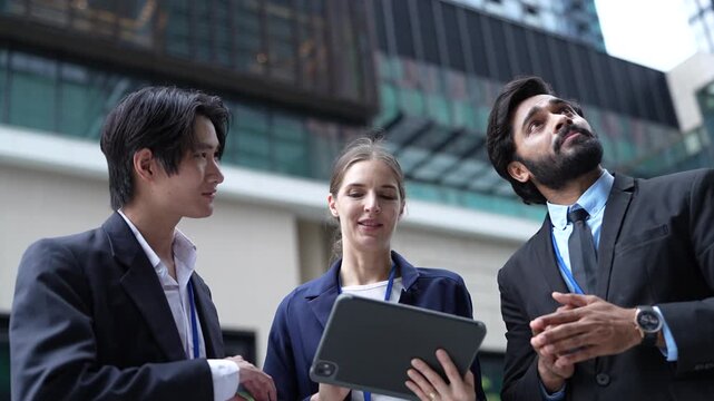 Three business colleagues with a digital tablet discuss a project outdoors while one raises a hand to explain a point beside the polished facade of a new mixed use city development