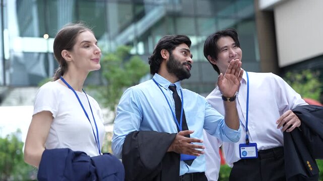 Three colleagues in shirtsleeves laugh together with their suit jackets folded over their arms outside a glass office tower in a modern Asian financial district