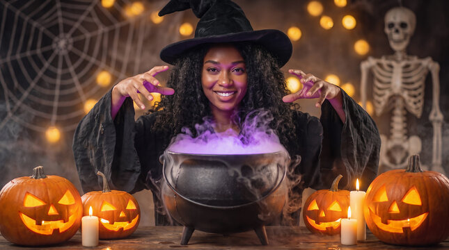 Young adult black woman in witch costume conjuring magic over a bubbling cauldron with jack-o-lanterns, candles and skeleton, Halloween