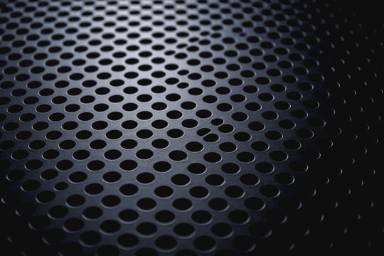 A close-up view of a dark perforated metal panel with uniform circular holes, showing industrial texture and precise pattern details.