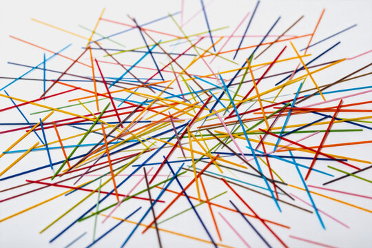 A collection of thin, colorful straight sticks arranged chaotically on a plain white background, forming an abstract pattern.