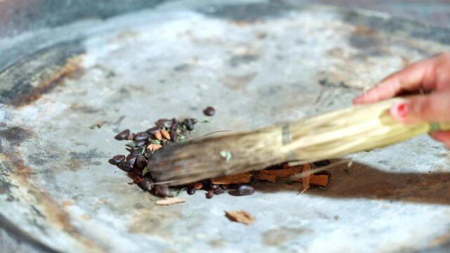Traditional preparation of tejate, a maize and cacao beverage from oaxaca, mexico, showing a woman's hands roasting and stirring cacao beans, spices, and herbs on a hot comal with a brush