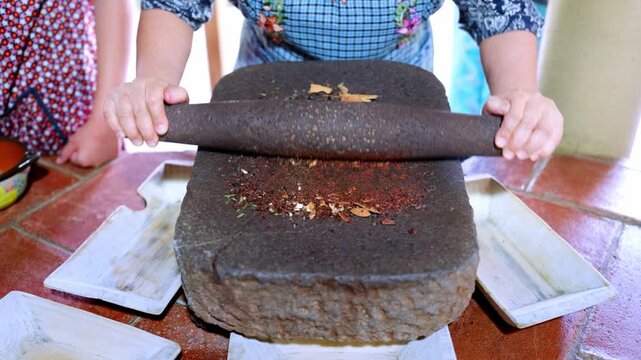 Female hands grinding various aromatic spices and cocoa beans on a traditional stone metate, showcasing an ancient culinary method for preparing authentic mexican mole from oaxaca