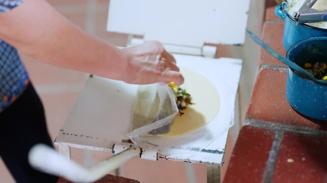 Woman's hands skillfully folding a fresh corn tortilla with a savory filling, crafting a traditional handmade empanada in an authentic oaxacan kitchen setting with a rustic tortilla press