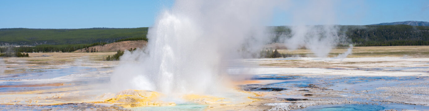 Clepsydra Geyser erupting with yellow minerals at base and small hot spring, sunny blue sky day, summer vacation at Yellowstone National Park viewing natural geothermal features
