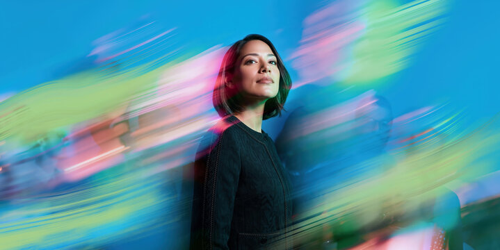 Confident Indian American Female Professional Standing Calm Amid Artistic Blue Green Pink Motion Blur