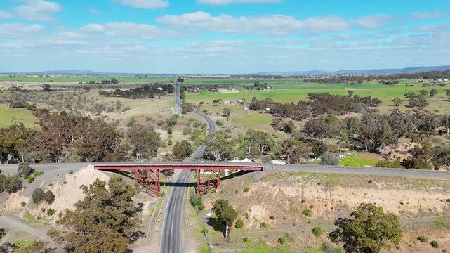 Aerial view looking along a regional road&nbsp;passing under a trestle railway bridge in Rowsley, Victoria Australia. Single-track rail overpass, surrounding rural farmland, and hills near Bacchus Marsh.