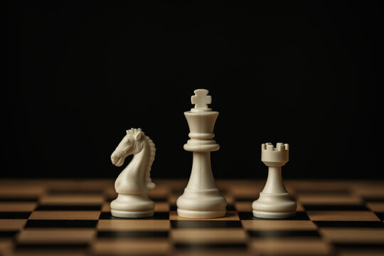 white chess pieces (king, knight, rook) aligned on wooden board, on black background