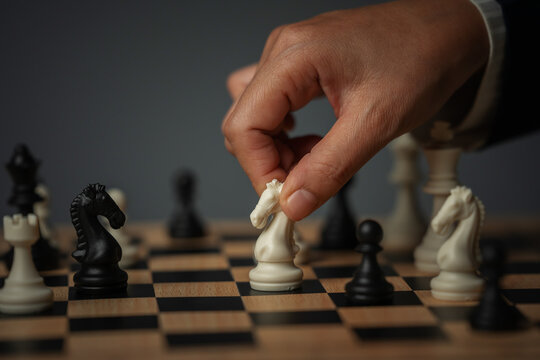 business hand moving white chess knight on wooden board during a game