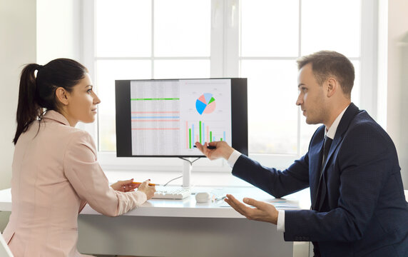 Businesswoman and businessman analysts discuss office data charts. He explains insights on a monitor, comparing revenue and KPI trends for planning in office. Clear finance teamwork growth idea.