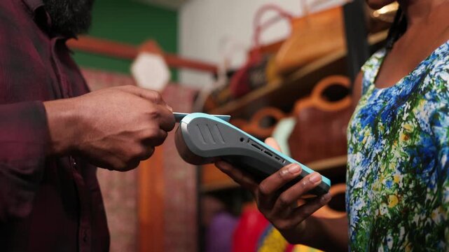 African woman small business owner processing card payment using POS terminal for a customer in her handbags shop