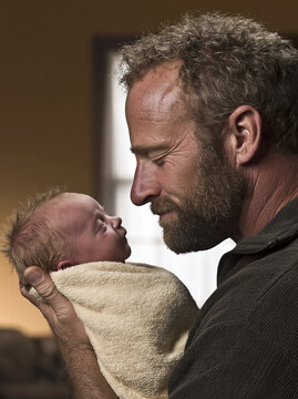 Father gently holding newborn baby wrapped in soft blanket, sharing tender moment at home