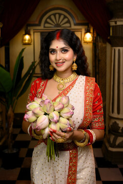 Portrait of beautiful Indian woman wearing a traditional red and white saree and jewellery, holding lotus flowers in her hand